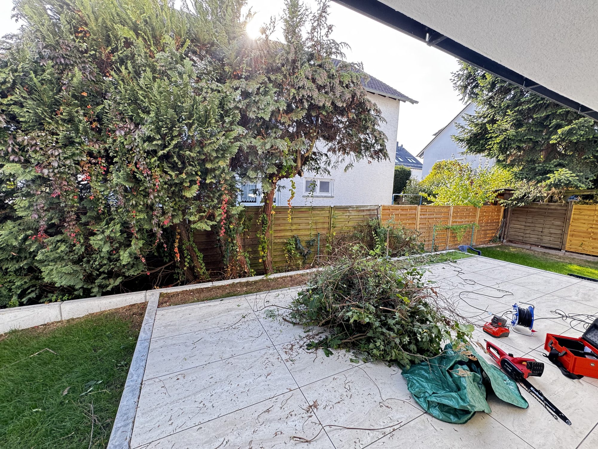 Terrasse vorher – zugewachsene Hecke, Schnittgut und Geräte auf der Fläche